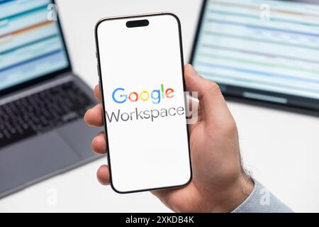 PRAGUE, CZECHIA - JULY, 2024: GoGoogle Workspaceogle Workspace logo on the screen of smartphone in mans hand and laptop on the background  Stock Photo
