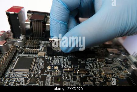 Computer technician replaces the flat battery on a battery-backed electronic board. 3-Volt lithium coin cell. Selected focus. Stock Photo