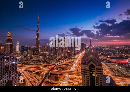 A panoramic view of Dubai's skyline at twilight, featuring the Burj Khalifa and other skyscrapers, with illuminated roads snaking through the city. Stock Photo