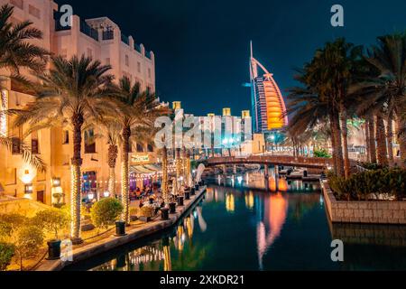 A view of a canal in Dubai at night, with a restaurant on the left and a tall building with lights reflected in the water. Stock Photo