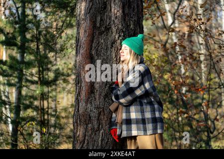 Grinning and relaxed woman meditating and basking in sun, enjoying walk in cold autumn woodland Stock Photo