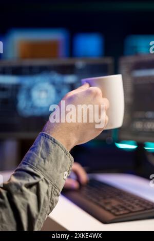 Man drinking coffee and updating artificial intelligence neural networks, writing binary code script. IT professional upgrading high tech AI, enjoying hot beverage, close up Stock Photo