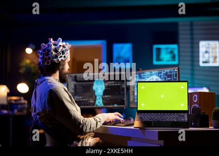 Software engineer with EEG headset starting mind upload trying to gain bionic powers, isolated screen on laptop. IT admin using high tech neuroscientific gear and chroma key notebook Stock Photo