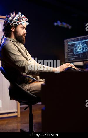 Programmer using EEG headset translating thoughts into PC commands using brainwave signals. Man controlling computer functions using his mind, helped by biosensor technology research Stock Photo
