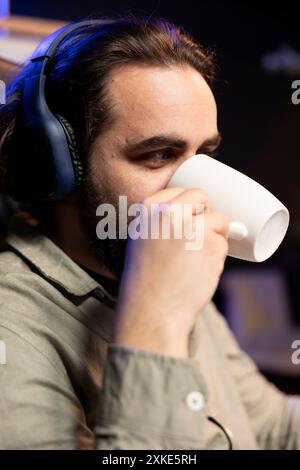 Computer engineer listening music and drinking coffee while updating artificial intelligence neural networks. IT professional enjoying music and hoy beverage, upgrading high tech AI in home office Stock Photo