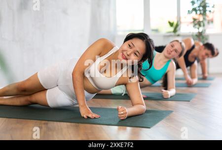 Diligent young women and man practicing upward boat pose of yoga on black mat in light fitness gym Stock Photo