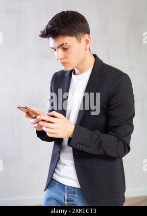 Calm guy in black jacket holds phone in hands uses Internet and communicates on social networks Stock Photo