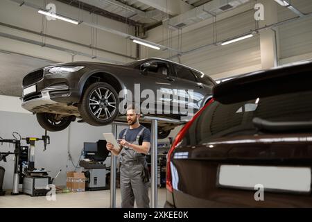 Mechanic using tablet while inspecting elevated SUV in garage Stock Photo