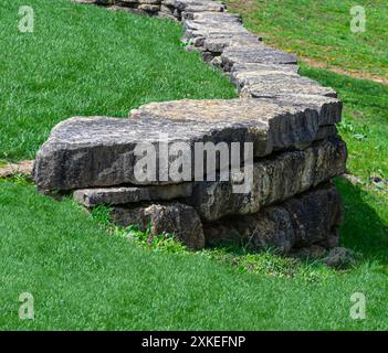 Retaining wall made of stacked flat rocks through green grass Stock Photo