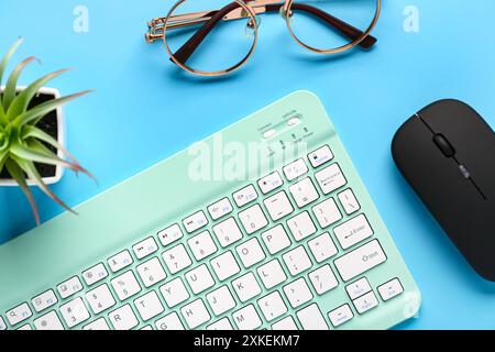 Eyeglasses, succulent, computer mouse and keyboard on blue background. Top view Stock Photo