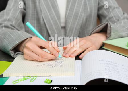 Woman writing math formulas in notebook at table, closeup Stock Photo