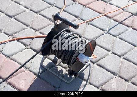Extension cord, electric cable on a reel on the grass for connecting garden tools, lawn mowers sunny day on lawn Stock Photo