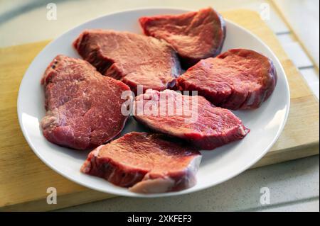 Multiple raw beef steaks are arranged on a white plate, prepared for seasoning and grilling Stock Photo