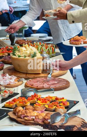People are serving themselves from a table full of italian cured meat, cheese and other delicious food during a catered event Stock Photo