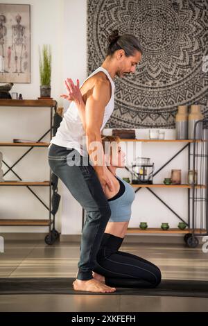 Side view of flexible fit female doing stretching exercise with personal fitness instructor during workout Stock Photo