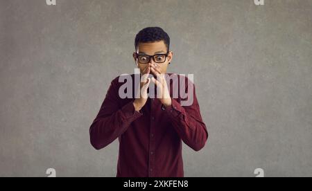 Portrait of emotional scared african american young man standing on gray background. Stock Photo