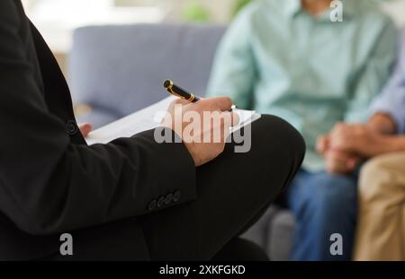 Professional family therapist taking notes on clipboard during conversation with married couple Stock Photo