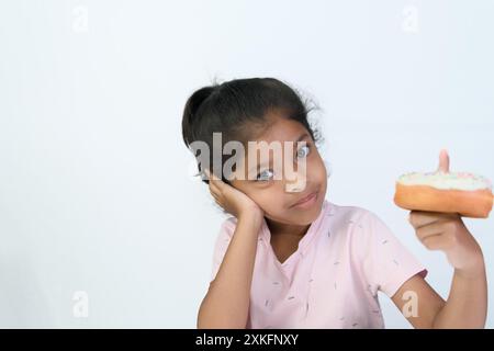 This little girl's contemplating if she should really eat that tempting donut. Stock Photo