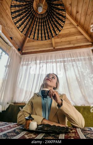 Woman Gazing Upwards While Enjoying a Drink in a Cozy Cafe Stock Photo
