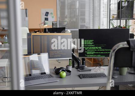 Background shot of programmer desk setup with laptop and computer screens displaying source code in empty software development agency office Stock Photo
