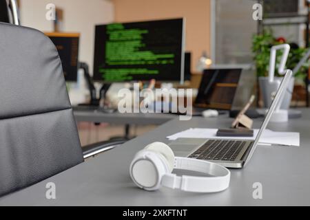 Side view of laptop with headphones on desk in empty computer programmer office, background shot, copy space Stock Photo