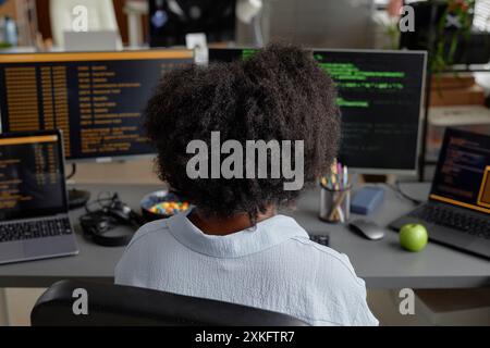 Rear view of female programmer of Black ethnicity working on multiple computers reading screen with software code lines running Stock Photo