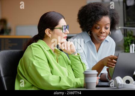 Young smiling African American woman pointing at computer screen while assisting higher-weight junior IT specialist in coding, problem solving discussion Stock Photo