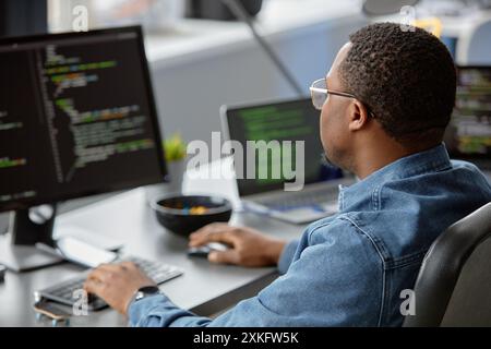 Back view of male African American IT engineer focused on writing code looking at computer screen on blurred background, copy space Stock Photo