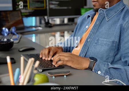 Cropped shot of male African American software developer writing code working at desk with multiple computer screens while having fingerboard at hand in programmer office, copy space Stock Photo