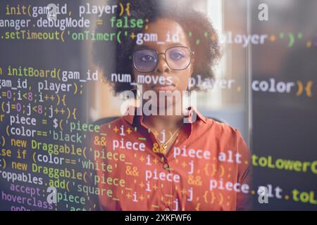 Creative shot of serious female software developer of Black ethnicity reflecting in computer screen with code lines running Stock Photo