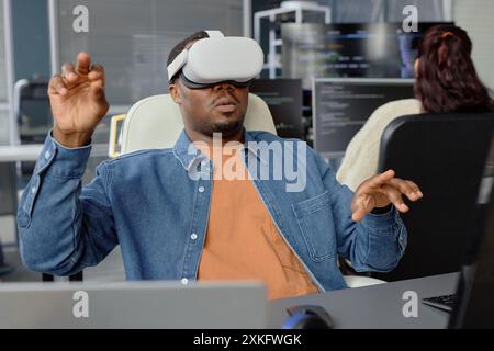 Male African American software developer testing VR application or game wearing headset fully immersed in virtual desktop experience Stock Photo