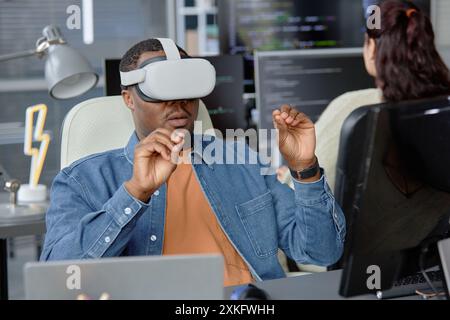 Male African American software engineer in headset using VR systems and virtual desktop at working desk in office Stock Photo