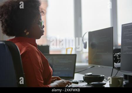 Side view of concentrated female African American IT engineer code programming on computer writing script while sitting at desk against window in office, copy space Stock Photo