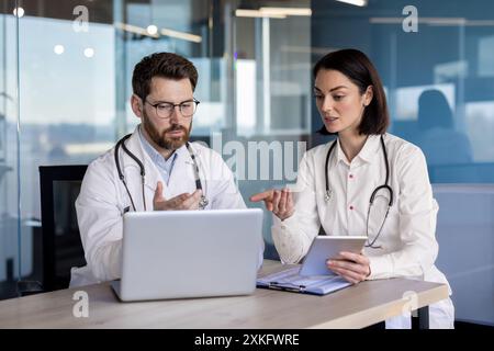 Medical professionals in discussion about patient information using laptop and tablet in modern office setting. Team of healthcare workers collaborating, consulting, and reviewing medical data. Stock Photo