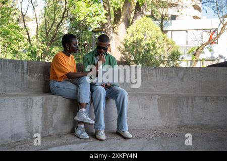 Thoughtful boyfriend, girlfriend classmates using computer to study sitting on campus stairs outside Stock Photo