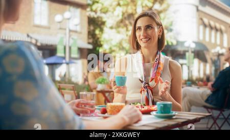 Two Happy Girlfriends Having a Fun Conversation on a Terrace. Friends Meeting For Lunch in an Italian Style Outdoors Cafe. Young Women Talking, Telling Work Stories, Chatting About Family Stock Photo