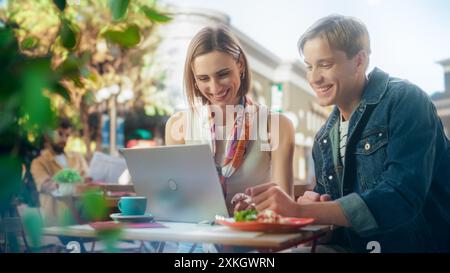 Two Office Workers Having a Work Lunch in a Cafe. Young Female Manager and Male Specialist are Sitting on a Terrace, Discussing a Marketing Project and Analyzing Financial Data on a Laptop Computer Stock Photo