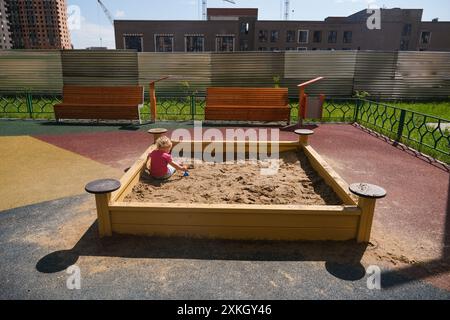 Child playing in the sandbox in the playground in the courtyard of a house Stock Photo