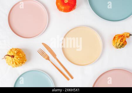 Ceramic plates with fork and knife and pumpkins on white tablecloth. Top view, mockup. Stock Photo