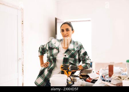 A young woman stands at a table with construction tools. A charming girl in casual clothes is making repairs in the apartment. A worker among building Stock Photo