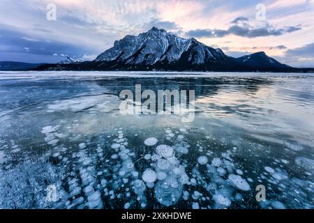 Landscape of natural bubbles frost on frozen Abraham Lake with rocky mountains in winter at Kootenay Plains Area, Alberta, Canada Stock Photo