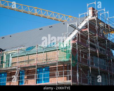 Partial view of scaffolding on a newly constructed multi-story building with brick cladding and yellow crane boom against a blue sky. Stock Photo