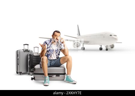Worried tourist at the airport sitting on a suitcase and using a mobile phone isolated on white background Stock Photo