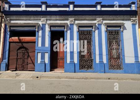 531 One-storey Eclectic house of white facade with blue moldings, intricate grille windows, roll-up garage door, on Calle Corona Street. Santiago-Cuba Stock Photo