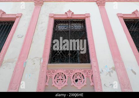 538 One-storey, Eclectic style house with chipped white facade and pink moldings, intricate grille windows on Calle Santa Rita Street. Santiago-Cuba. Stock Photo