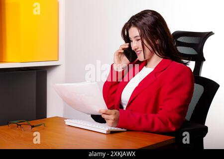 business and company concepts. businesswoman in red coat makes phone call and reviews documents. business management and empowered woman Stock Photo
