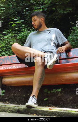 A vivid image featuring a young tattooed man in sporting clothes, looking bored and waiting on a bench on a sunny day in the city of Zurich. Stock Photo