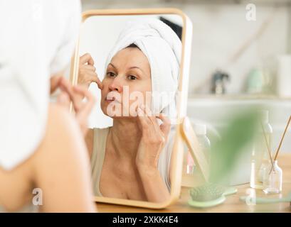 Middle-aged woman examining her facial skin looking in the mirror put on the table Stock Photo