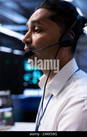 Data center agent supporting engineering team doing hardware maintenance, talking in headset microphone. Worker in high tech server room facility coordinating technicians using mic Stock Photo