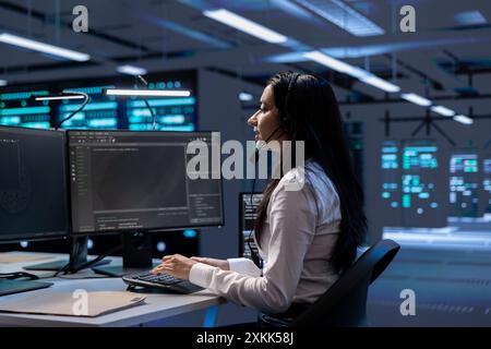 Data center support expert supporting engineering team doing equipment maintenance, talking in headset microphone. Woman in server farm coordinating technicians using mic Stock Photo